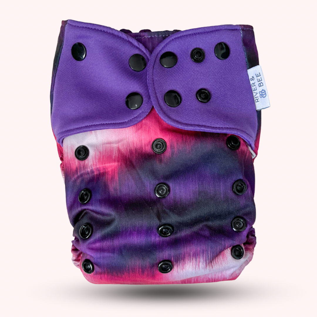 Photo: River & Bee modern cloth nappy in the print Aura. Pink and purple with black snaps.