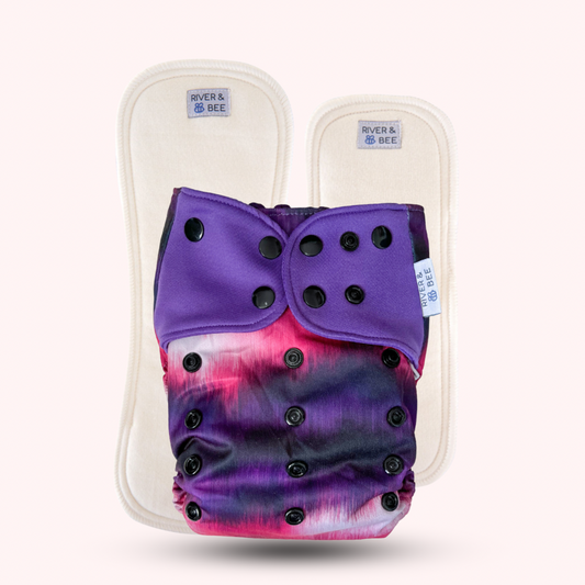 Image: River & Bee modern cloth nappy in the print Aura. Pictured with the premium insert set. Reusable nappy print is purple and pink with black snaps.